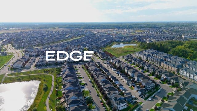 Aerial view of a suburban neighborhood with rows of modern houses, green spaces, and water bodies, showcasing community development and residential living environments.