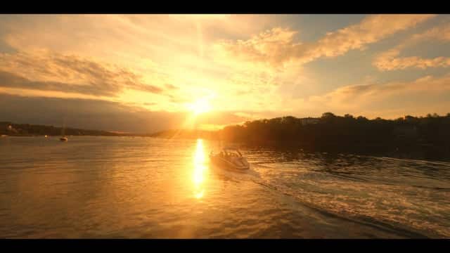 Sunset over a river with a boat speeding by during golden hour, creating a beautiful reflection on the water. Scenic outdoor landscape captured in vibrant sunset colors, ideal for travel and nature photography.