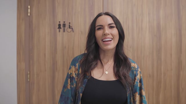 Vibrant young woman smiling in front of a wooden restroom door with accessibility symbols, showcasing candid moments for entertainment and lifestyle content.