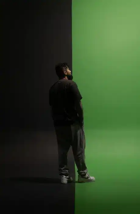 A person standing and looking at a split background with black on the left and green on the right, creating a striking visual contrast.