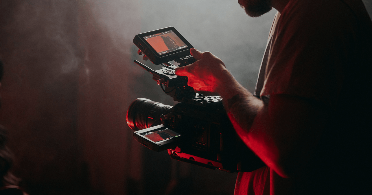 Filmmaker using professional camera equipment for video production, focusing on capturing high-quality footage in a dimly lit environment.